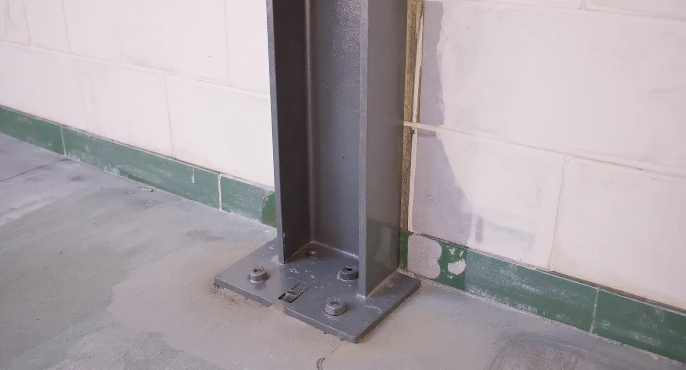Steel I-beam base plate connection detail showing anchor bolts securing plate to concrete floor slab for lateral load transfer to foundation footing